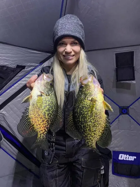 Nicole holding two crappie inside an ice shelter